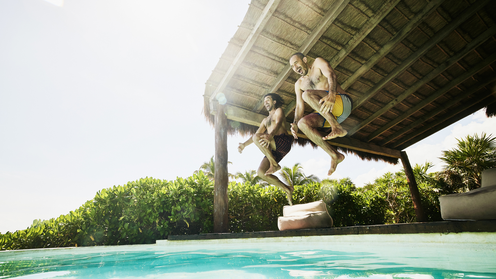 两名男子抱膝跳入泳池，溅起巨大水花