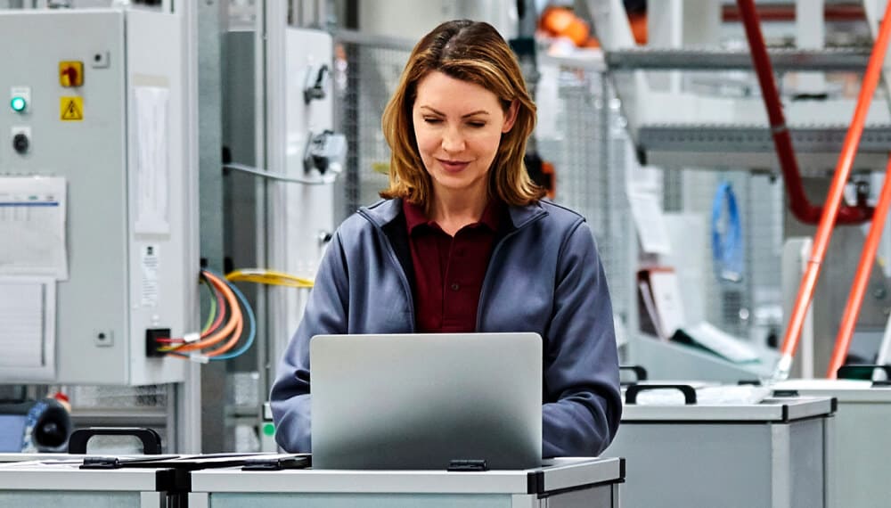 女经理在工厂内使用笔记本电脑操作 Infor MES 系统进行车间管理
