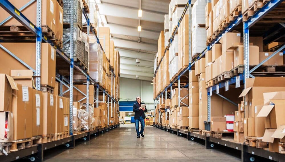 商人拿着平板电脑走在供应链仓库的过道上